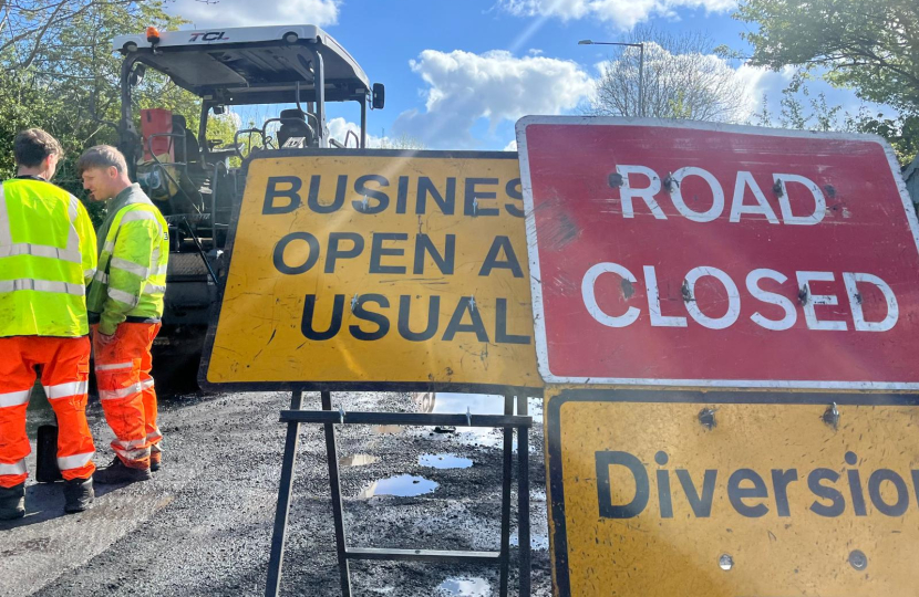 Road resurfacing work with road signs and workers visible