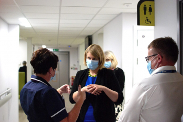 Katherine in medical setting talking to staff and wearing a medical mask