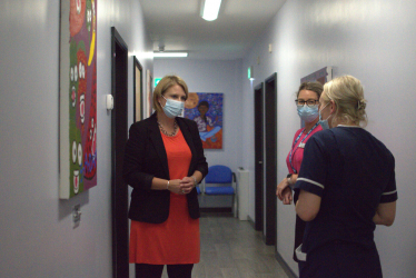 Katherine in medical setting talking to staff and wearing a medical mask